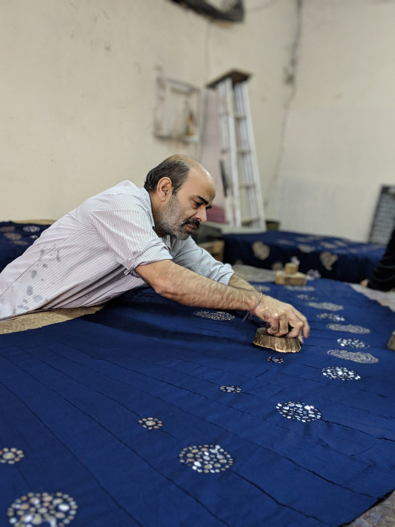 A printer pressing a carved block onto indigo cloth.