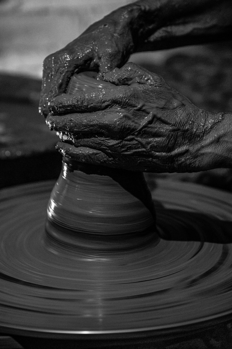 A potter's hands shaping clay, black and white.