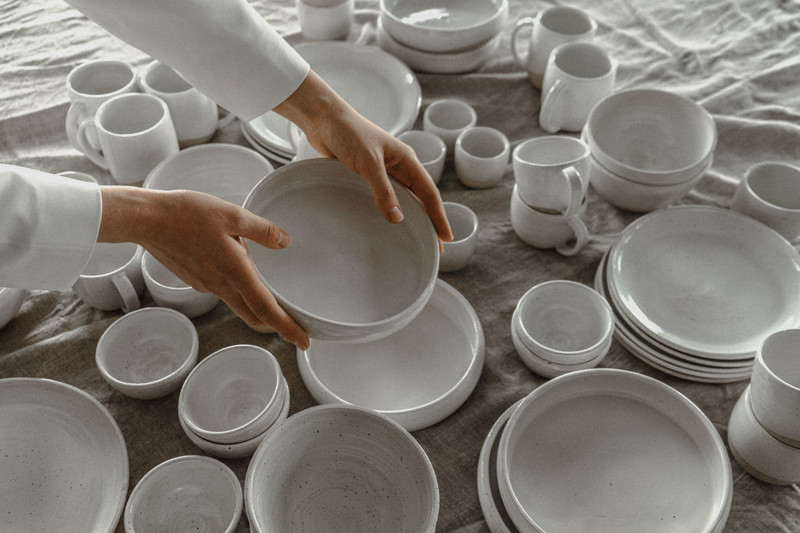 Hands arranging white plates and bowls.