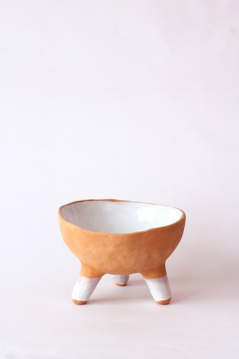 A terracotta bowl on three white legs.