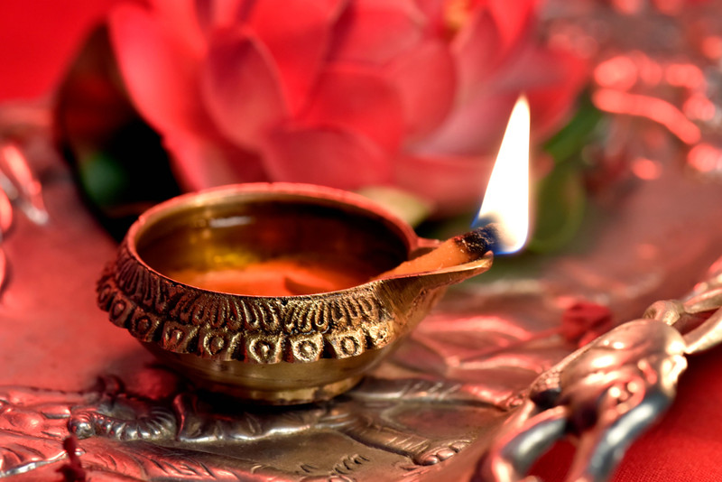 A lit brass diya on a silver tray.