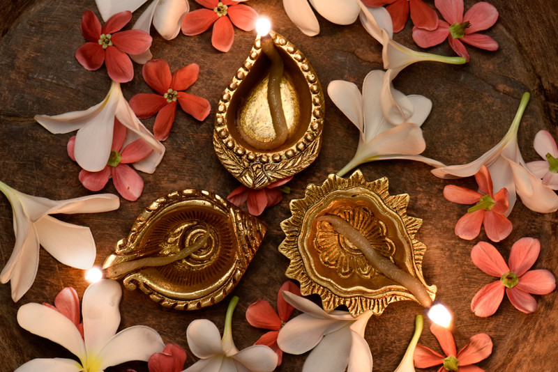 Brass diyas lit among flowers.