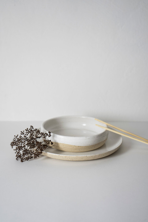 A white rice bowl on a plate with chopsticks and dried flowers.